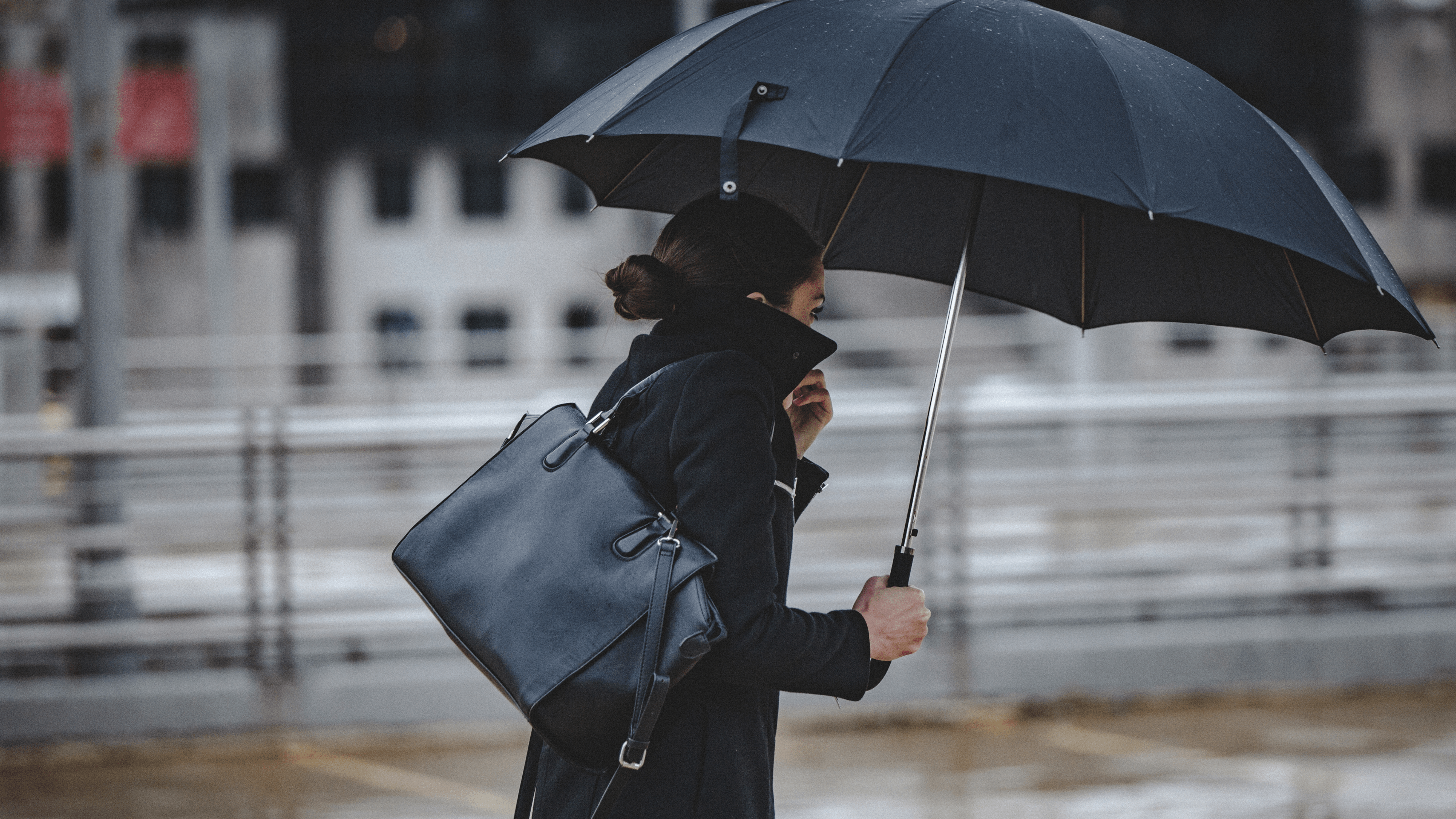 A woman walks down the street, holding an umbrella and struggling with the wind on a cold and rainy day.